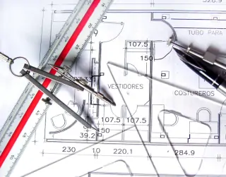 Photo of a drafting board with a ruler, compass and set squares on top of it.